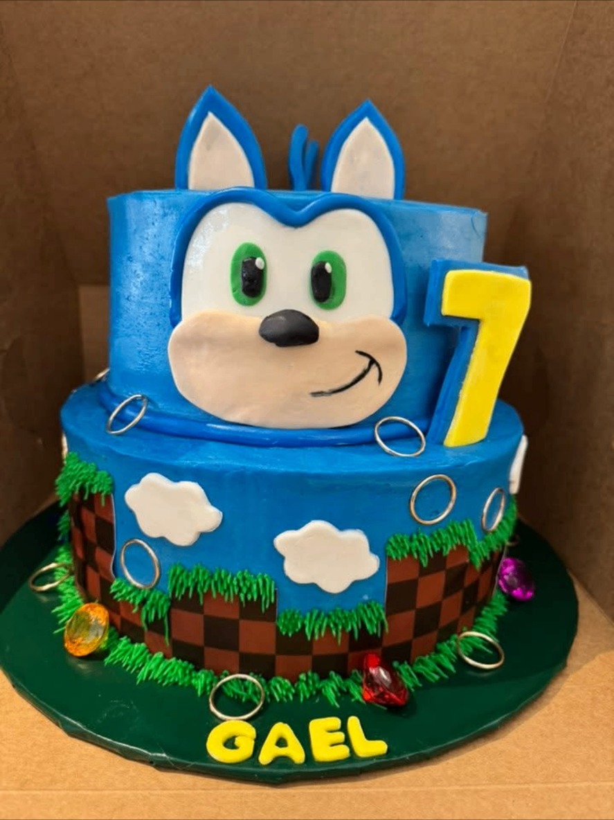 Two-tier blue birthday cake with a cartoon hedgehog face and gold rings